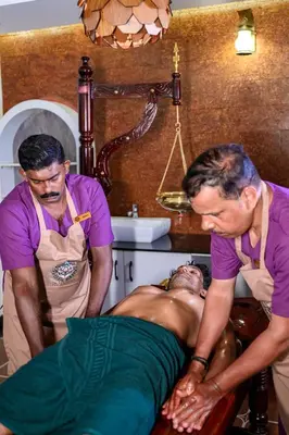 two men standing around a man laying on a bed at Dr Indulekhas Ayurvedic Wellness And Rejuvenation in Tellicherry