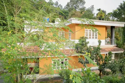 an orange house with trees in front of it at Namastay - Haritha Thara in Kalpetta