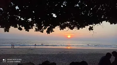 a sunset on a beach with people in the water at Peaceful Homestay near Kizhunna Beach in Thottada