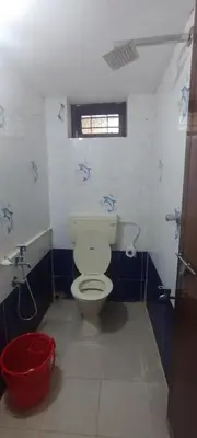 a bathroom with a toilet and a red bucket at Raya Casa Couple Suite 101 in Guruvāyūr