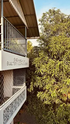 a sign for a building next to a bush at Snehanilayam in Trichūr