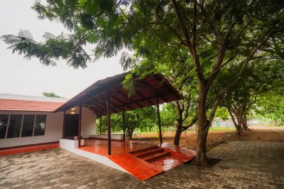 a pavilion with a tree in front of a house at Vetha farm in Aravakkurichchi