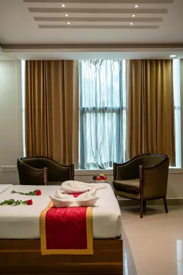 a room with two beds and two chairs and a window at Royal Plaza Glitz Inn in Kozhikode