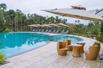 a swimming pool with chairs and an umbrella at EVORA Resort and SPA in Ambalavayal