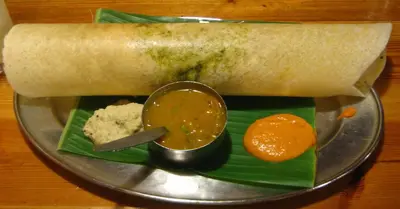 a plate with a bowl of food on a banana leaf at Suvarna Residency in Mysore