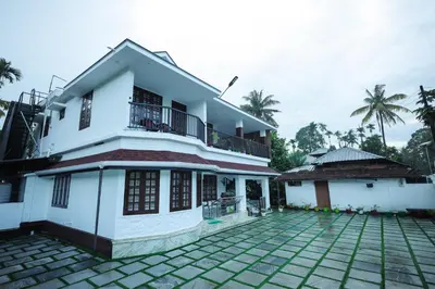 a white house with a balcony and a courtyard at Wayanadan Huts Homestay in Sultan Bathery