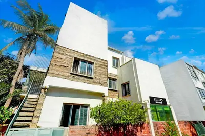 a white building with a palm tree in front of it at Hotel O Mysuru Sand Museum in Mysore