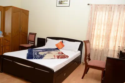 a bedroom with a bed with two chairs at Rainbow Cottages-Budget Friendly rooms in Ooty
