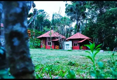 two small red buildings in a field with trees at THE DOCkSIDE INN in Madikeri