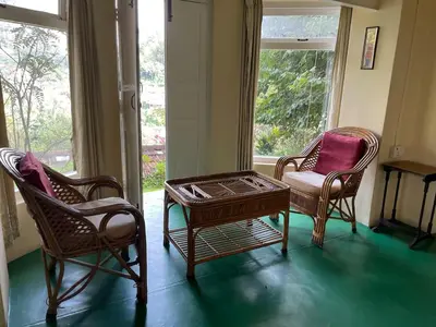 two chairs and a coffee table in a room with two windows at Glenwood in Coonoor