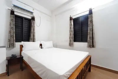 a bedroom with a large white bed and two windows at Hotel O Coimbatore Brookefields Mall in Coimbatore