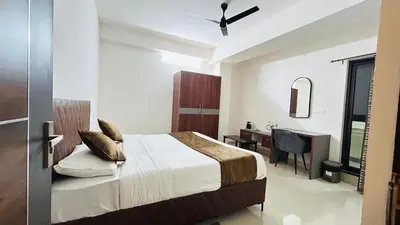 a bedroom with a bed and a desk and a window at Queens Suite Rooms in Channapatna