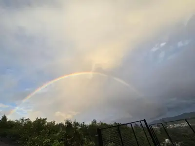 a rainbow in a cloudy sky with a fence at Indhraprashtham in Aruvankadu