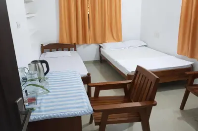 a room with two beds and a table and chairs at Gods Gift Homestay James Inn in Kozhikode