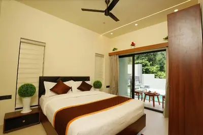 a bedroom with a bed and a balcony with a table at LA VILLA Resort in Vythiri
