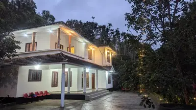 a white house with red chairs in front of it at Lush Lagoon Homestay in Ambalavayal