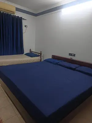 a bedroom with two beds with blue sheets and a window at Poonthanam guest house in Guruvāyūr
