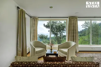 a living room with a couch and chairs and large windows at StayVista at Sande's Farview with Bonfire in Coonoor