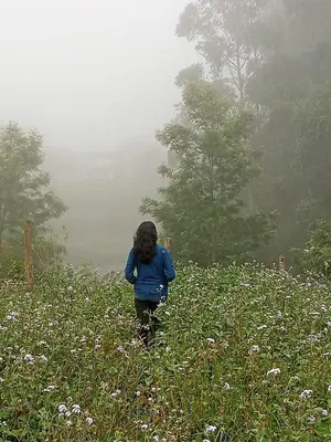 a woman walking through a field of flowers at Lone Tree Creek in Vattavada
