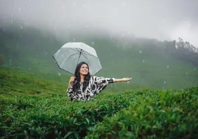 a woman holding an umbrella in the rain at Arivikad Tea Bungalow Munnar By VOYE HOMES in Munnar