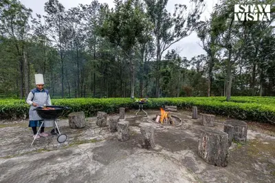 a man standing next to a grill and a fire at StayVista at Farview Suite Serenity with Lawn in Kotagiri