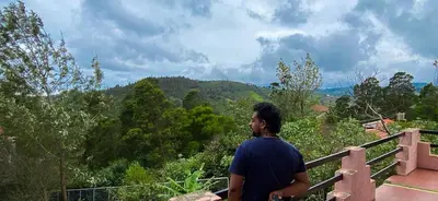 a man standing on a balcony looking out at the mountains at Willostays Cloudhill ooty in Ooty