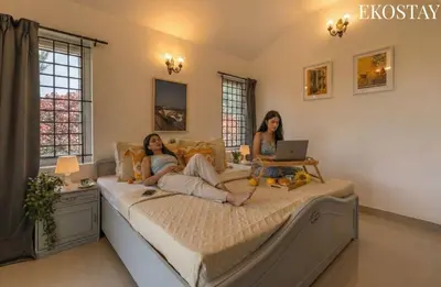 two women sitting on a bed with a laptop at EKOSTAY - Villa Eve in Ooty