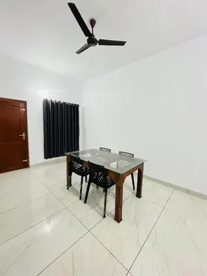 a table and chairs in a room with a ceiling fan at CT HOMESTAY, Omassery in Tāzhekkod