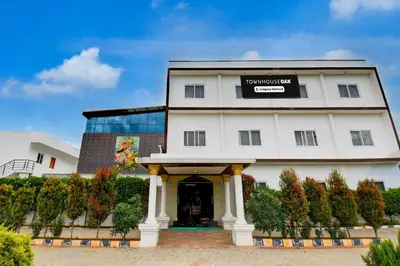 a white building with a sign on it at Super Townhouse Oak Sri Mahadeshwara Convention Centre Formerly Shri Aprameya Resort in Mysore