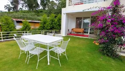 a white table and chairs on a lawn with flowers at Mayfield Valley Homestay in Kotagiri