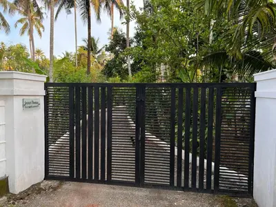 a black iron gate with palm trees in the background at Cottage on Riverside in Irinjālakuda