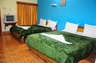 two beds in a hotel room with a tv at Hotel Zaraa in Ooty