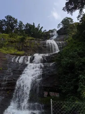a waterfall on the side of a mountain with a fence at Jungle View Homestay Anakulam in Viripara
