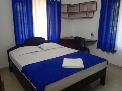 a bedroom with a bed with blue curtains and a desk at Ocean blue home stay in Pallipuram