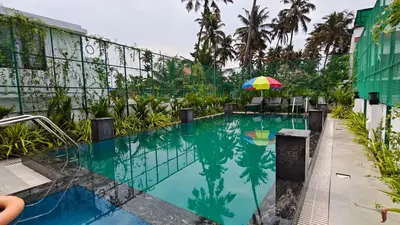 a swimming pool with an umbrella and chairs and a building at Cherai Beach Regency in Ernakulam