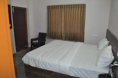 a bedroom with a bed and a chair and a window at Parvathi comforts inn in Mysore