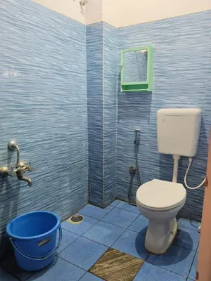 a blue tiled bathroom with a toilet and a bucket at love moon home stay in Mysore