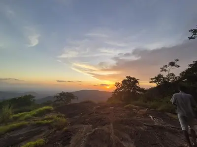 a man standing on top of a mountain looking at the sunset at Mamalakandam Green Hill Stay in Diya Homesay in Mamalakandam
