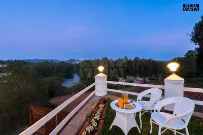 a balcony with two chairs and a table and lights at The Lake House Ooty in Ooty