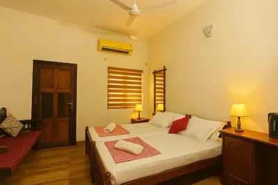 a bedroom with a bed with white sheets and red pillows at Haris Farm House in Kannur