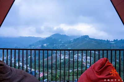 a person sitting on a balcony looking at the mountains at Zostel Kodaikanal, Vilpatti in Kodaikānāl