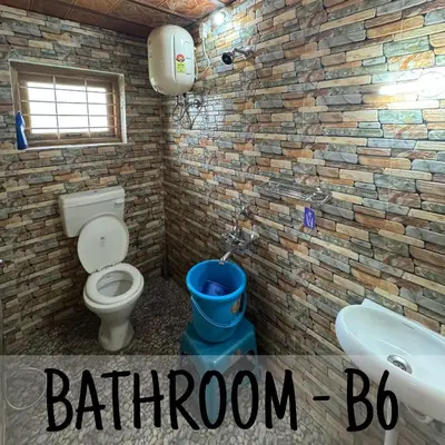 a bathroom with a toilet and a blue bucket at Ambassador Inn in Kodaikānāl
