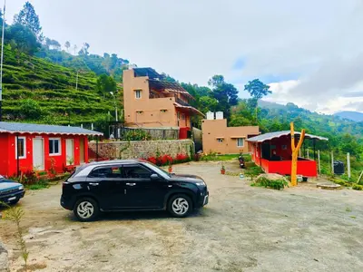 a black car parked in a parking lot next to houses at Humming Bird By Brown Tree Resorts in Kotagiri