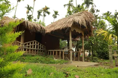 a house with a straw hut with palm trees at Vihara Mudcamp in Marayoor