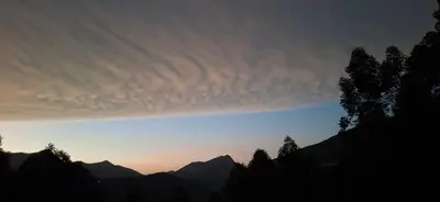 a cloudy sky at sunset with trees and mountains at Dadysmud house in Kottakamboor
