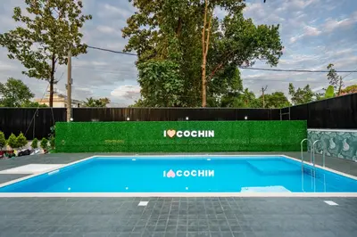 a blue swimming pool next to a green fence at Victoria Suites Airport Hotel in Nedumbassery