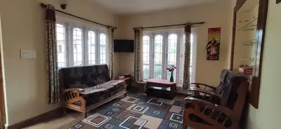 a living room with a couch and two windows at Nivriti Cottage Valley View Stay in Ooty
