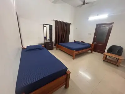 a bedroom with two beds and a chair in it at Anugraha inn in Guruvāyūr