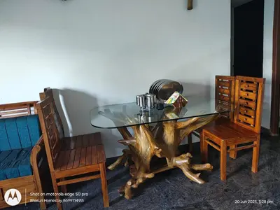 a glass table with a tree stump base and two chairs at Bhasuri Non-AC Room in Agali