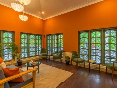 a living room with orange walls and windows at The Hosteller Bam Coorg in Madikeri